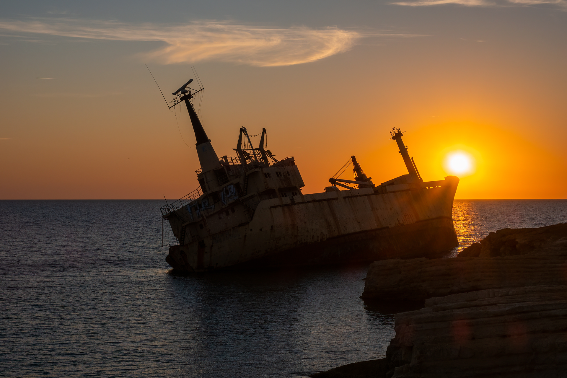 A mesmerizing view of the Peyia sea caves with the Edro III shipwreck in the backdrop, set against a fiery red sun's descent